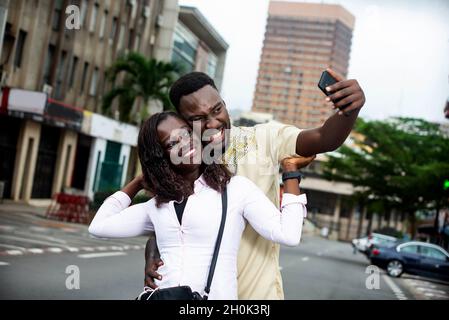 young couple standing outdoors photographing themselves with mobile phone while smiling. Stock Photo