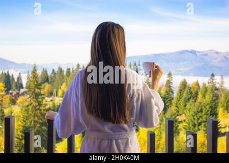 Brunette girl long hair from back in bathrobe standing on balcony. Tea cup drink Stock Photo