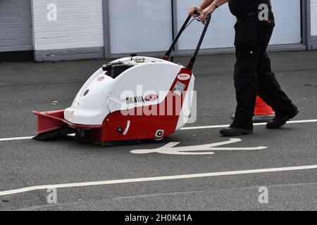 A man cleaning a path on a walkway with a handheld sweeping machine Stock Photo