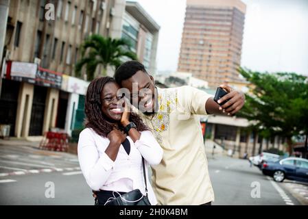 young couple standing outdoors photographing themselves smiling. Stock Photo