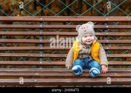 Cute little one-year-old child on a park bench. Portrait of a smiling toddler boy. Walking in the autumn park