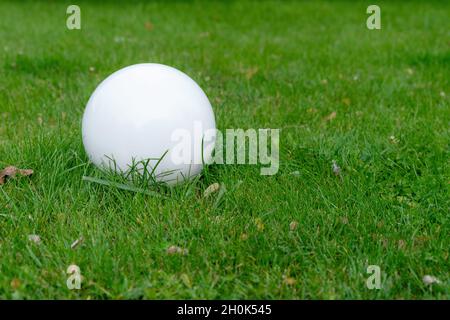 Lighting ground street lamp in the shape of a ball mounted on a green lawn in the park. Street round white lanterns. Copy space for you text Stock Photo