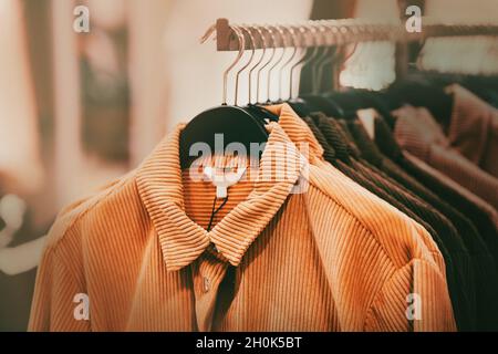 Beautiful corduroy coats for the autumn season in ginger and brown colors hang on hangers in a clothing store in the mall. Shopping. Stock Photo
