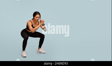 Workout concept. Sporty african american lady doing deep squats exercise, training over blue background, panorama Stock Photo