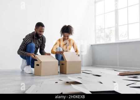 Smiling young african american family preparing for move, stack cardboard boxes for things in living room interior Stock Photo