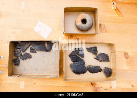 Taarstedt, Germany. 13th Oct, 2021. Pieces of pottery and the weight of a loom (above) lie on a table as finds in cardboard boxes during excavations. During the development work for a new building area, employees of the State Archaeological Office had come across a settlement from the time around 500 AD. (to dpa 'Archaeologists find 1500 year old remains of a settlement') Credit: Frank Molter/dpa/Alamy Live News Stock Photo