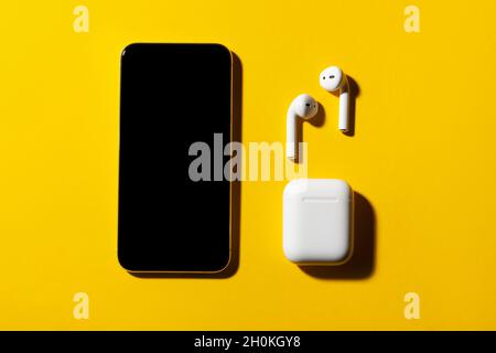 Smartphone and wireless headphones on yellow background. Stock Photo