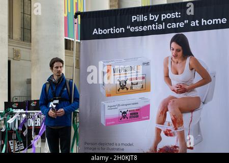 Tory Party Conference. Protester with banner text Pills by Post. Abortion Essential Care at Home. Woman sat on toilet with blood.