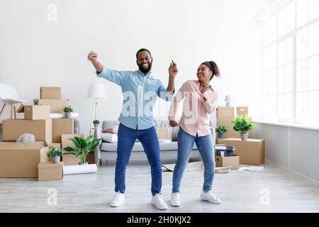 Satisfies excited young african american lady and guy dancing in living room with cardboard boxes with things Stock Photo