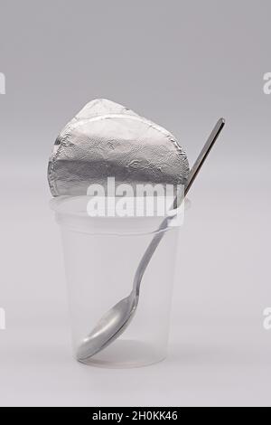 empty, transparent yoghurt cup with opened aluminum foil and stainless steel spoon isolated against a white background Stock Photo