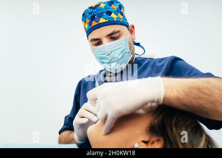 Professional male dentist wearing mask and gloves while treating a female patient in dental office. Stock Photo