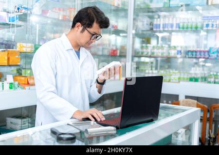 Portrait of young male pharmacist holding medication while using laptop at pharmacy counter Stock Photo