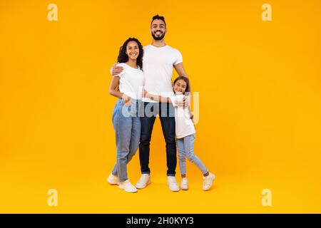 Middle-Eastern Parents And Daughter Embracing Expressing Positive Emotions, Yellow Background Stock Photo