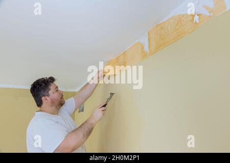 Manual work with scraper preparation for painting a room worker hand scraping wallpaper on wall Stock Photo