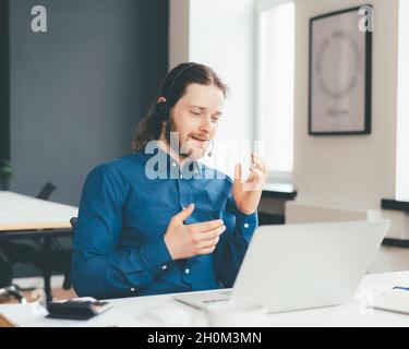 Smiling young male manager in headset and formal wear chatting with client on laptop in office Stock Photo