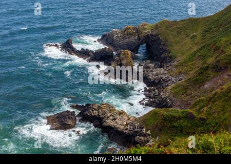Rock arch and coastline in summer on the South West Coast Path at Lizard Point in south Cornwall England UK. Stock Photo