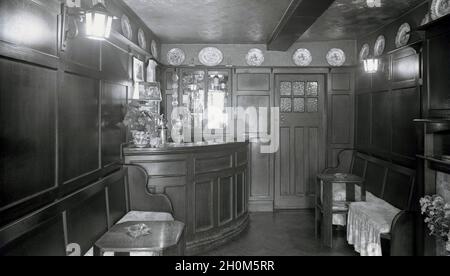 1950s, historical view of a small, cosy 'snug' pub bar at a British country tavern or inn, with teak wood paneling and traditional pub items such as decorative plates on display, The Angel Inn, Market Square, Witney, Oxford, England, UK, Stock Photo