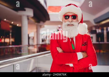 Photo of confident funny santa folded arms prepare x-mas gifts wear sunglass hat red tuxedo in supermarket mall center Stock Photo