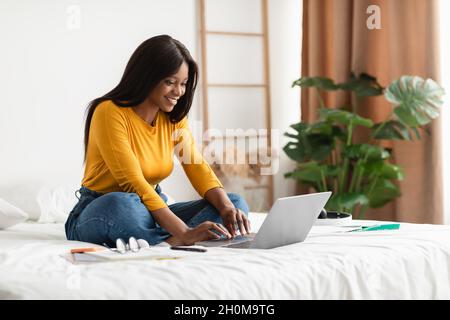 Black Young Woman Using Laptop Typing Sitting In Bedroom Indoors Stock Photo