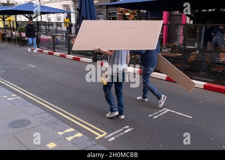 With their heads and faces obscured by their load, two workmen carry construction boards through Covent Garden in the West End, on 12th October 2021, in London, England. Stock Photo