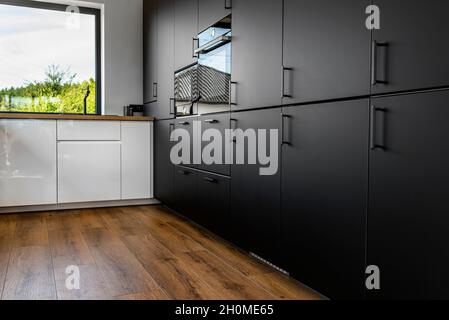 Modern kitchen with black fronts, built in oven and microwave, vinyl panels on the floor. Stock Photo
