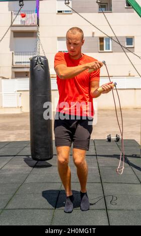 Strong and muscled young man jumping and using rope for that. Guy is calm and concentrated on doing excercise. He is alone there. Stock Photo