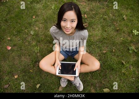 Cheerful young woman using her tablet computer on the lawn Stock Photo