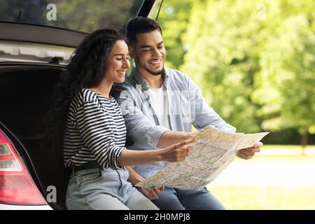 Happy lovers sitting on car trunk and watching map Stock Photo
