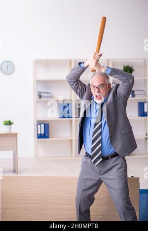 Old businessman employee holding baseball bat in the office Stock Photo