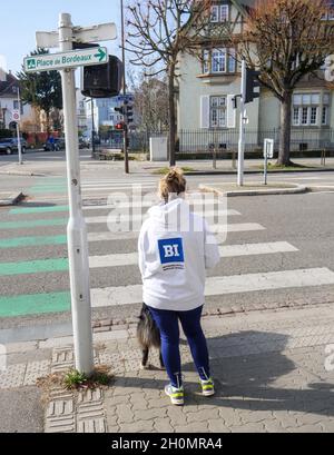 woman with a dog waiting for green light at street crossing with hooding showing Bi Norwegian Business School slogan Stock Photo