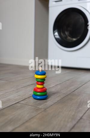 An improperly assembled multi-colored childrens pyramid stands on the floor in the laundry room against the background of a washing machine Stock Photo