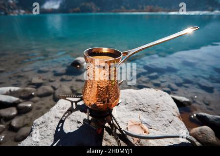 Copper Cezve for coffee in autumn lake camping in the mountains. Preparing coffee on gas stove outdoor camping concept Stock Photo