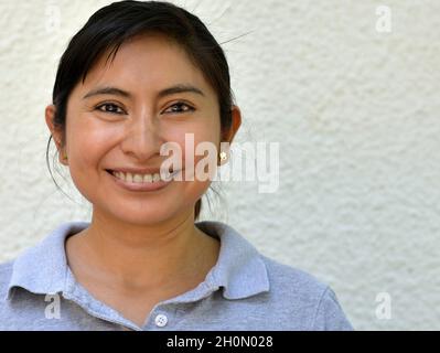 Young optimistic positive confident Mexican Caucasian Latina woman with brown eyes smiles and looks at the viewer in front of grey background. Stock Photo
