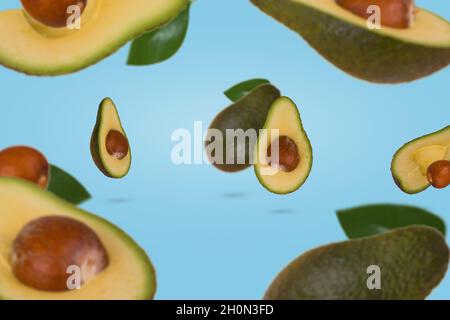 Creative scene with fresh ripe whole and sliced avocado flying in air isolated on blue background. Healthy food, diet, tropical exotic fruit, trendy f Stock Photo