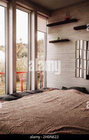 Vertical view of a cozy bed in front of a large window on the whole wall with a view of the lake Stock Photo