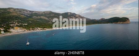 Aerial view of Jaz Beach promontory in the background. Budva. Montenegro. Catamaran. Jagged coasts with sheer cliffs overlooking the transparent sea. Stock Photo