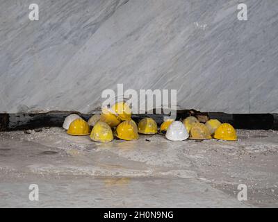 Yellow Work Protective Helmets Resting on the Ground in front of a Marble Slab: Marble Quarry Workers. Stock Photo