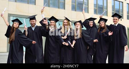 graduate students in black student robes and square hats are happy to receive diplomas and finish the educational process. Stock Photo