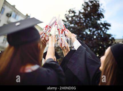 group of university graduates in student robes or mantle and square hats at the graduation ceremony hold college graduation certificates in their Stock Photo