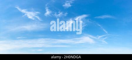 Clear azure sky with few wispy cirrus clouds. Sparse translucent white clouds in the blue sky on a sunny day. Concepts of weather forecast, vacations. Stock Photo