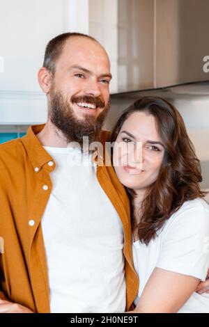 Happy family couple portrait husband and wife in kitchen. Couple of young middle aged man and woman. Young Smiling bald caucasian man hugging his wife Stock Photo