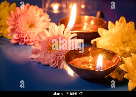 Happy Diwali. Burning diya oil lamps and flowers on blue background. Traditional Indian festival of light. Celebrating religious holiday. Stock Photo