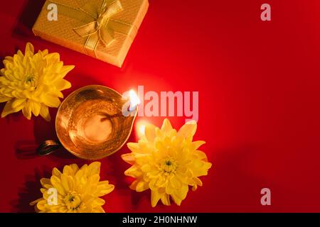 Happy Diwali. Diya oil lamp, flowers and gift boxes on red background. Celebrating the Indian traditional festival of light. Copy space. Stock Photo
