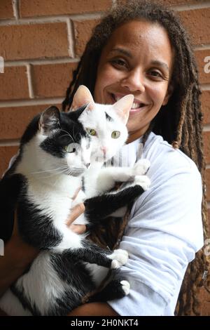 Woman smiles while holding two cats Stock Photo