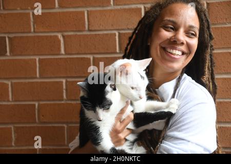 Woman smiles while holding two cats Stock Photo