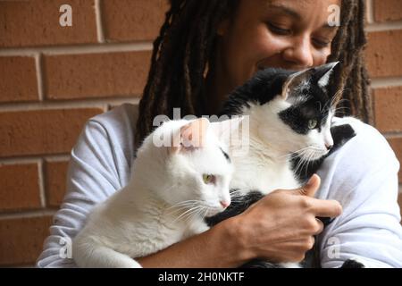 Woman smiles while holding two cats Stock Photo