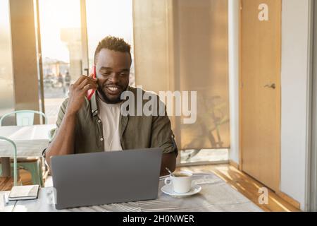 Young worker african man doing business call with mobile phone while working inside coffee restaurant - Focus on face Stock Photo
