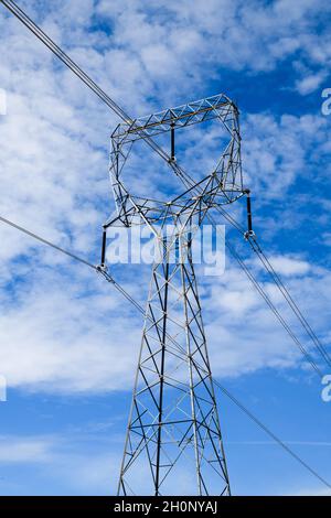 A high voltage transmission tower stands tall against a blue sky scattered with white clouds on a sunny day.  The wires hang from insulators Stock Photo