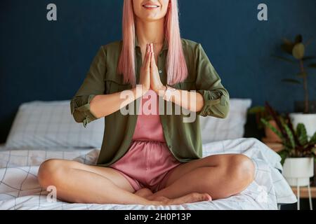 Smiling female model meditates holding hands in namaste mudra on large bed closeup Stock Photo