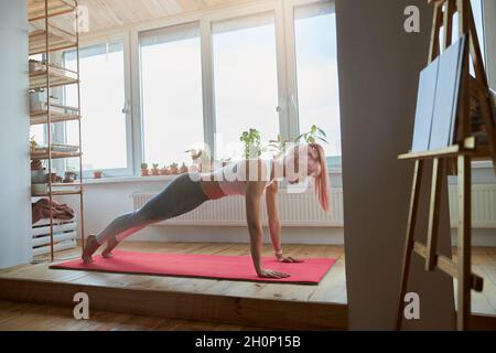 Concentrated woman stands in plank on mat on spacious balcony Stock Photo